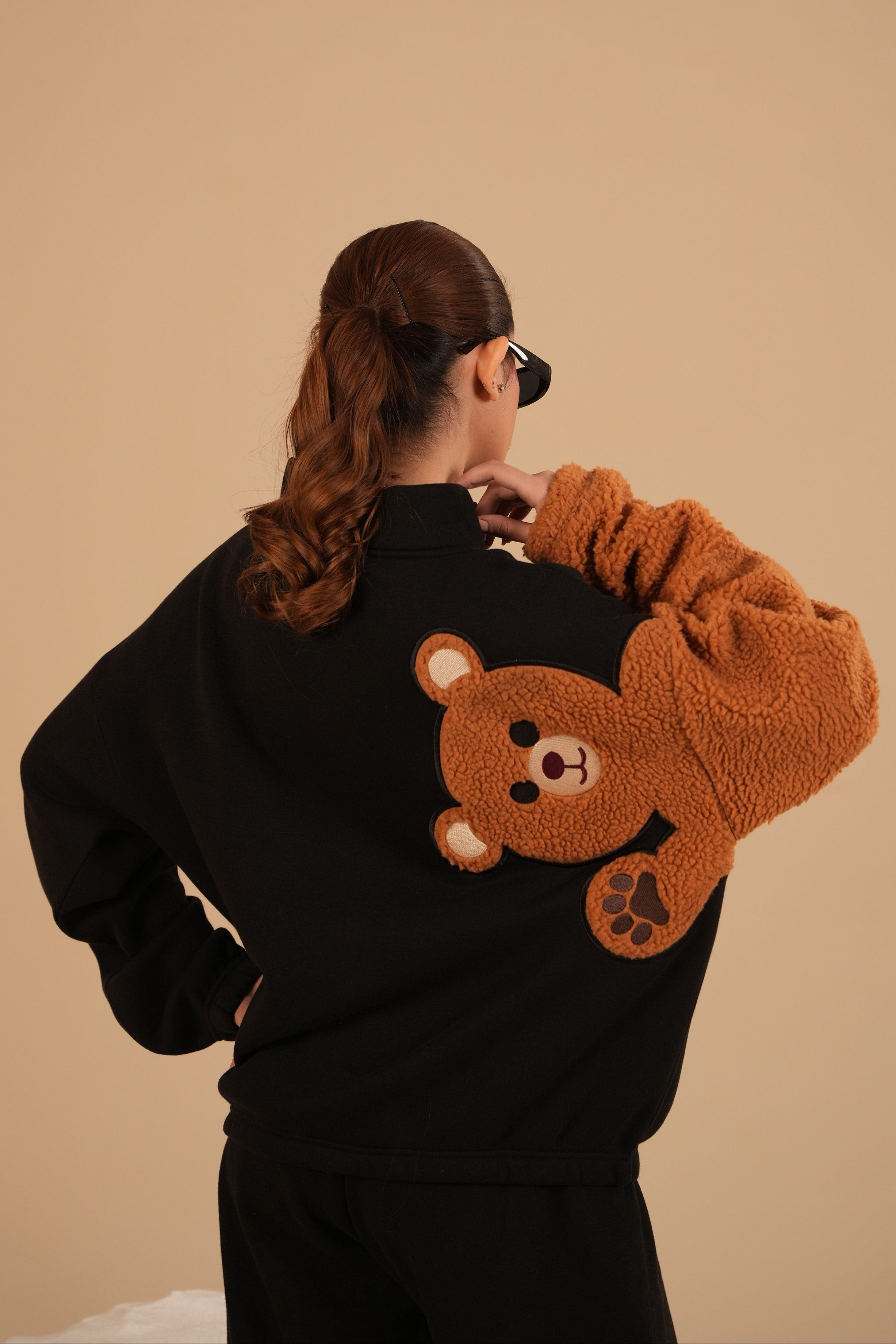 Person wearing a black hoodie with a brown bear design on a beige background